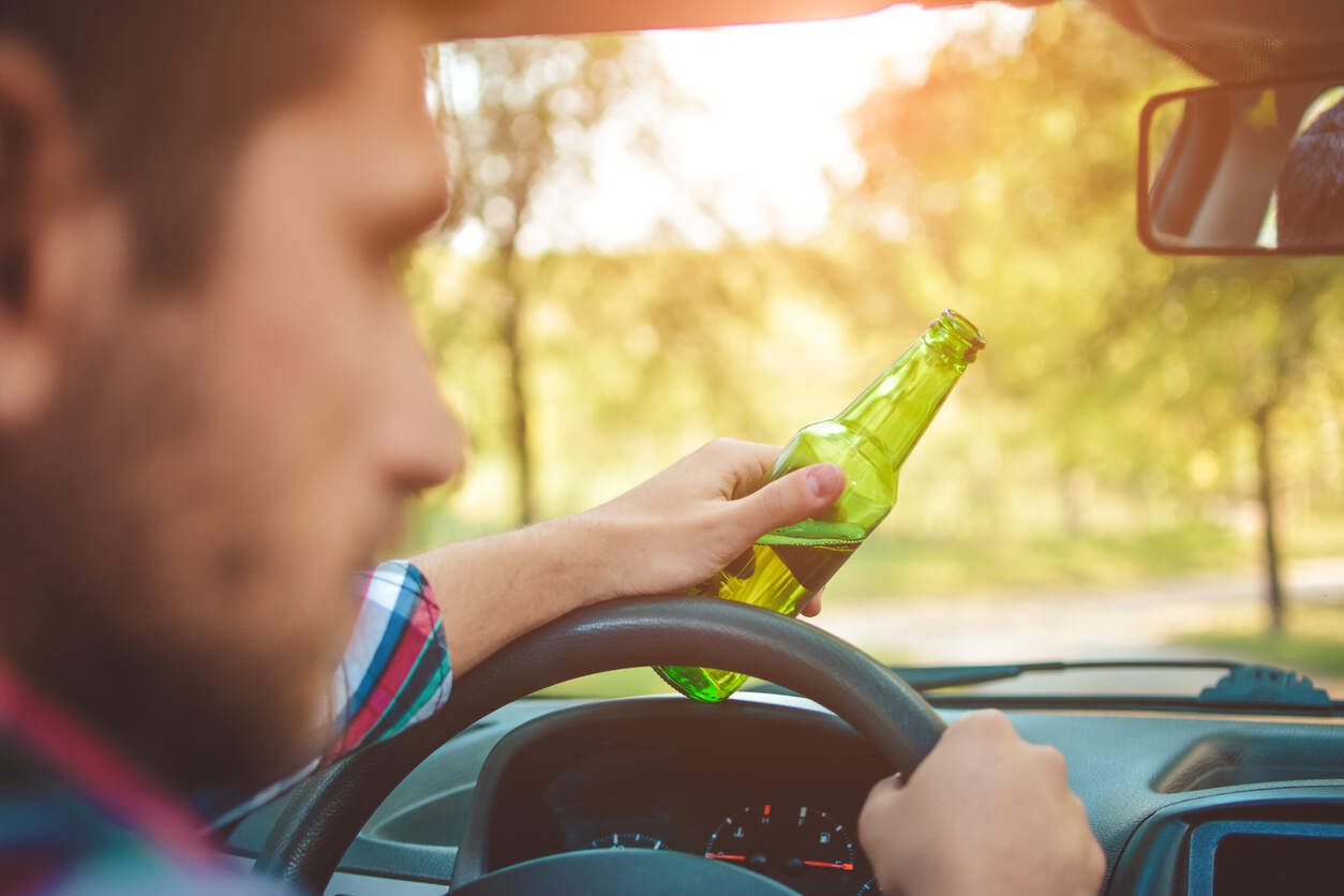 Driver holding beer bottle at steering wheel, representing a San Jose drunk driving accident lawyer.
