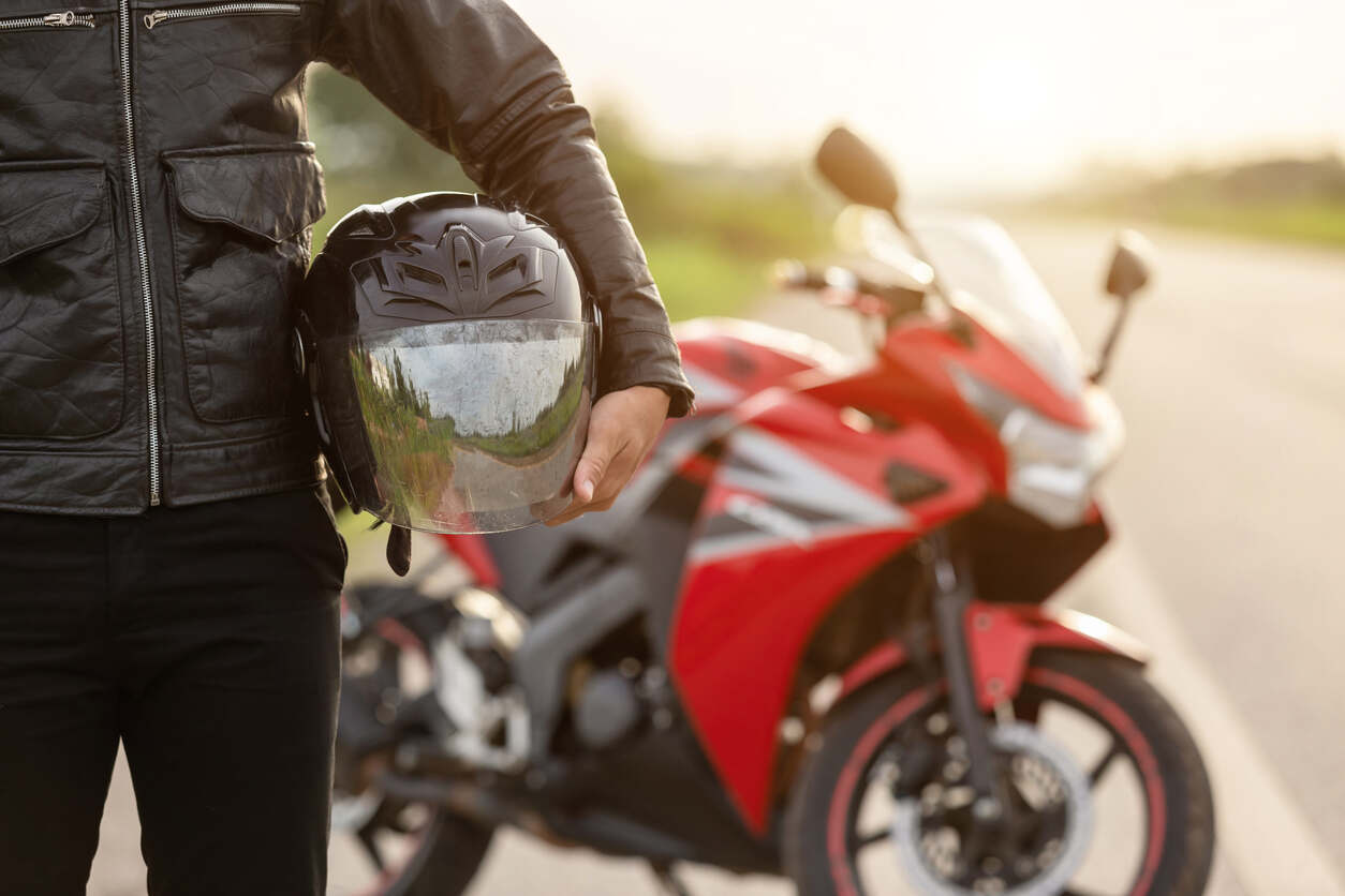 Motorcycle rider in leather jacket holding helmet, illustrating San Jose motorcycle helmet laws