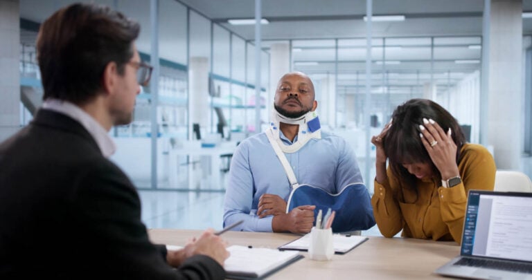 An attorney taking notes while meeting an injured client and his partner
